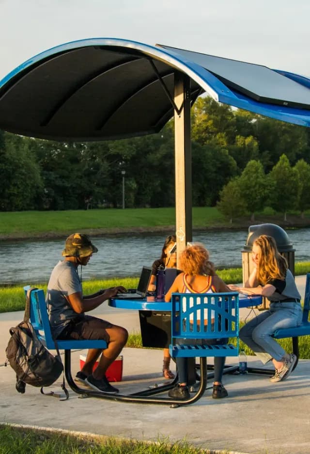 Friends at a shaded solar picnic table beside a river